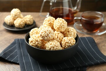 Tasty puffed rice balls in bowl on wooden table, closeup