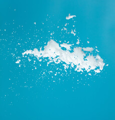 Snow dust element falling over blue sky. Fluffy White snow splash flying or throwing in mid air. Snowfall on blue background isolated