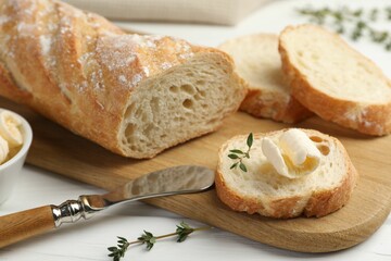 Cut baguette with butter and herbs on white wooden table, closeup