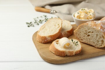 Cut baguette with butter and herbs on white wooden table, closeup