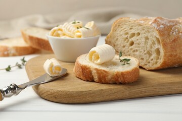 Cut baguette with butter and herbs on white wooden table, closeup