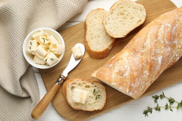 Cut baguette with butter and herbs on white wooden table, flat lay