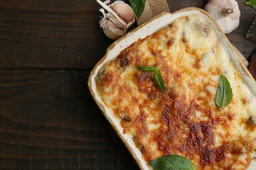 Delicious cooked lasagna in baking dish, basil and garlic on wooden table, top view. Space for text