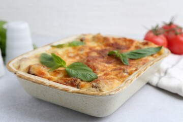 Delicious cooked lasagna in baking dish and basil on light grey table, closeup