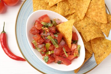 Delicious salsa (Pico de gallo) served with nachos and chili pepper on white wooden table, flat lay