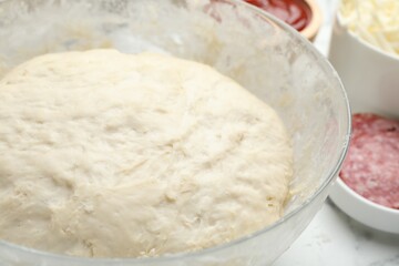 Dough in bowl on white table, closeup