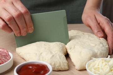 Making calzone pizza. Woman cutting dough into pieces at wooden table, closeup