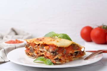 Piece of delicious cooked lasagna with basil on white table, closeup