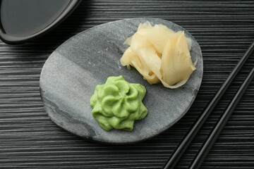 Hot wasabi paste, soy sauce, ginger and chopsticks on black textured table, flat lay