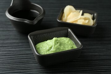 Hot wasabi paste, soy sauce and ginger on black textured table, closeup