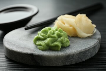 Hot wasabi paste, chopsticks and ginger on black textured table, closeup