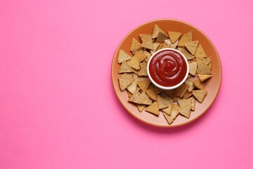 Ketchup in bowl and pieces of dry bread on pink background, top view. Space for text