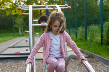 Little girl with long hair climbing on playground in summer. Healthy active mischievous child...