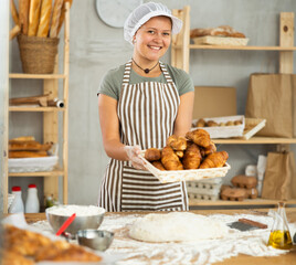 Home production of bread and pastries, work room, storage room. Young woman baker are standing near product range, hold croissants. Girl work in baking and selling bread products