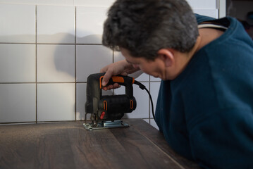 A woman is using a jigsaw to cut openings for electrical appliances into the kitchen countertop.