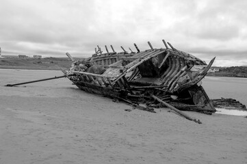 A large ship is laying on the beach, with its hull broken and its sails torn
