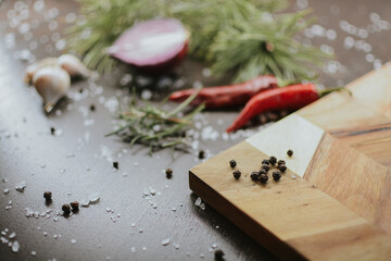 Coarse pepper on a wooden tray with salt, garlic, red onion, red pepper and rosemary for the chef