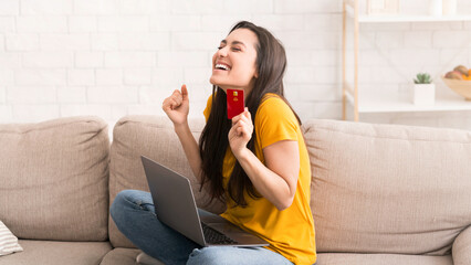 Online shopping. Emotional millennial girl with bank card and laptop computer buying something via...