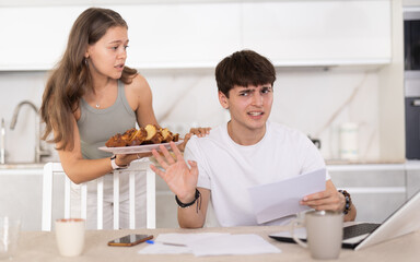 Young woman offering pie to young guy working on laptop in kitchen at home
