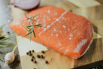 Fresh red salmon on wooden tray with coarse pepper, salt, garlic, red onion, red pepper and rosemary