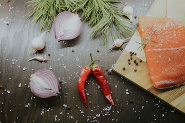 Fresh red salmon on wooden tray with coarse pepper, salt, garlic, red onion, red pepper and rosemary