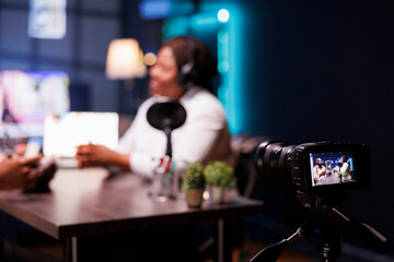 During an online show, african american couple is recording themselves with modern camera. Influencers are wearing headphones and speaking into microphones while discussing in a podcast.