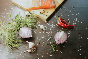 Fresh red salmon on wooden tray with coarse pepper, salt, garlic, red onion, red pepper and rosemary