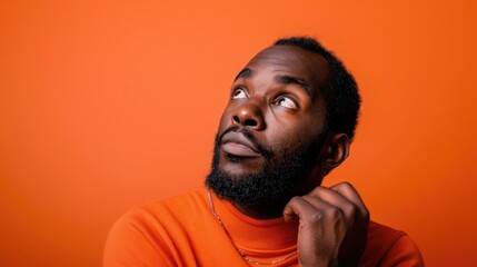 Fototapeta premium Man with a beard and dreadlocks is looking up at the camera. He is wearing an orange shirt and a necklace