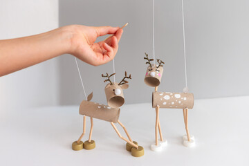Festive DIY reindeer puppets made from cardboard tubes and bottle caps held by hand with wooden stick. Minimalist Christmas craft. easy activity to do, paper roll craft for kid and kindergarten, 