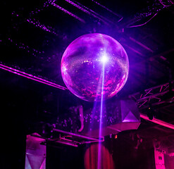 A shimmering disco ball illuminated by purple party lights hangs from the ceiling of a nightclub, creating a vibrant and festive atmosphere