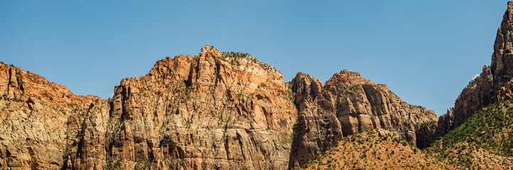 Fototapeta premium Panoramic view of tall desert canyon cliffs under a clear blue sky, showcasing the rugged sandstone formations in a scenic arid landscape