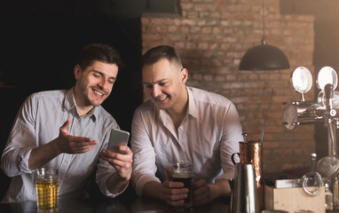 Two happy friends enjoying fresh beer at pub and browsing social networks on mobile. Technologies, online communication and internet addiction, copy space