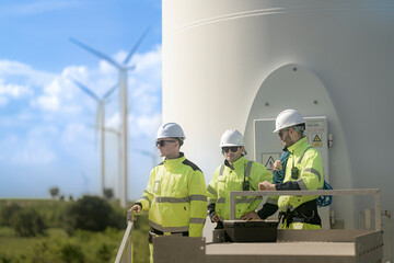 Fototapeta premium Two engineers stand on a platform, equipped with safety gear and ropes, in front of a wind farm. Wind turbines stretch across the background, showcasing the renewable energy infrastructure.