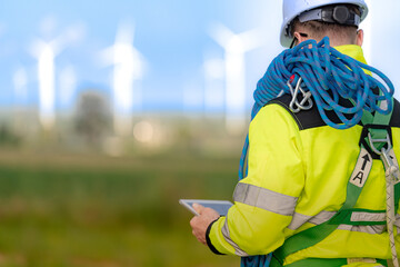 Two engineers wearing high visibility safety jackets and helmets measure wind speed with an...
