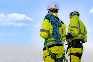 Two engineers wearing high visibility safety jackets and helmets measure wind speed with an...