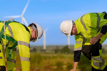 Two engineers wearing high visibility safety jackets and helmets measure wind speed with an...