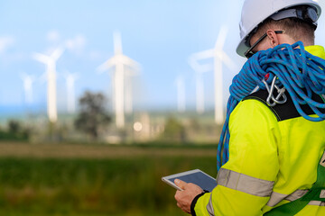 Two engineers wearing high visibility safety jackets and helmets measure wind speed with an...