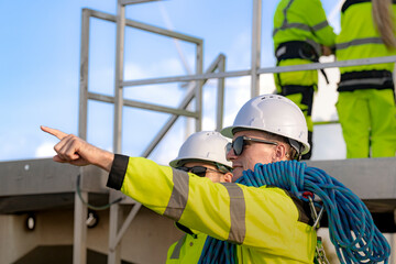 Two engineers in safety helmets and high visibility jackets engage in a field inspection. One is...