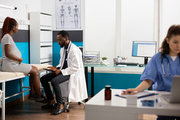 Obraz premium Image showcases multiethnic healthcare professionals using digital devices while pregnant woman sits on hospital bed. African american doctor discusses maternity care plan with young expectant mother.