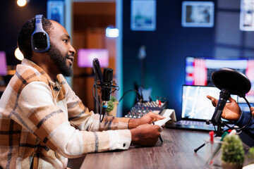 African american male journalist using his notebook and audio equipment to interview a person for...