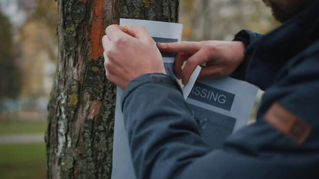 Lost pet owner sets dog photo poster of losing husky puppy on tree in park. Man pasting posters of the missing dog. Flyer with information about the missing dog hangs on a tree in the park. Lost dog.