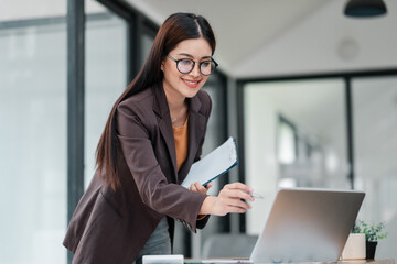 Professional woman in a stylish office setting, engaging with her laptop and paperwork, exuding confidence and focus.