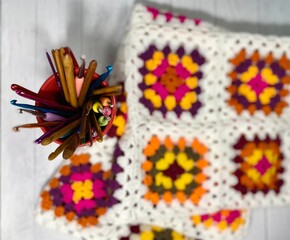 Collection of crochet hooks and bright multicolored colorful crocheted blanket made of granny squares cozy photo inside 