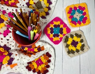 Collection of crochet hooks and bright multicolored colorful crocheted blanket made of granny squares cozy photo inside 