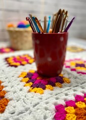 Many colorful multicolor wool balls in the basket on the table and collection of crochet hooks...