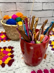 Many colorful multicolor wool balls in the basket on the table and collection of crochet hooks...