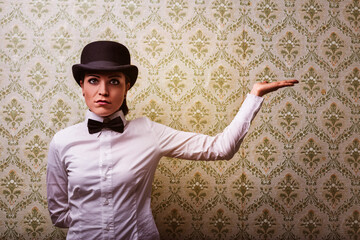 Young woman showing something wearing bowler hat and bow tie