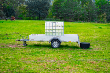 White Utility Trailer in Open Green Field with Water Container During Daylight