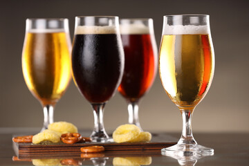 Glasses with different types of beer and snacks on mirror surface, closeup