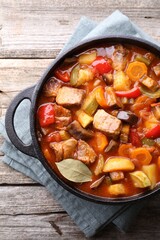 Delicious stew with vegetables in pot on wooden table, top view